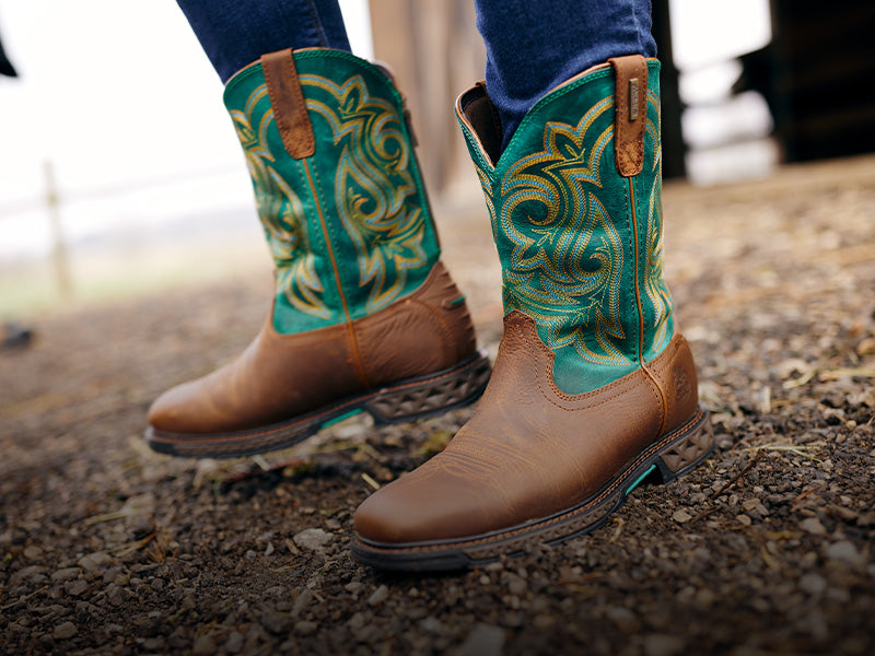 Close-up of brown and turquoise cowboy boots on a textured surface.