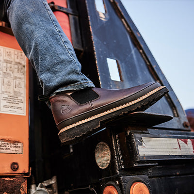 Person wearing brown work boots stepping onto a piece of machinery.