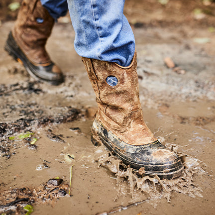 Brown work boots with visible brand logo on a muddy ground