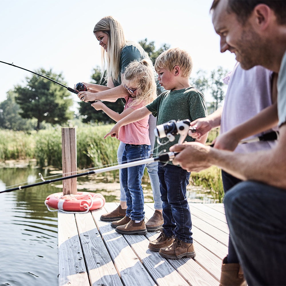 Family of four, including two adults and two children, fishing together on a wooden dock by a lake.