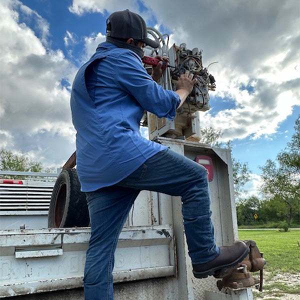 Person working on machinery in an outdoor setting with a truck and equipment.