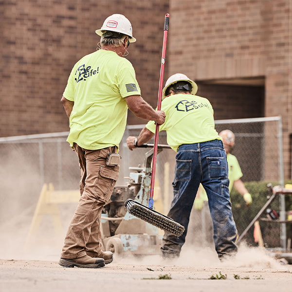 Two workers in high-visibility clothing using a machine on a construction site.