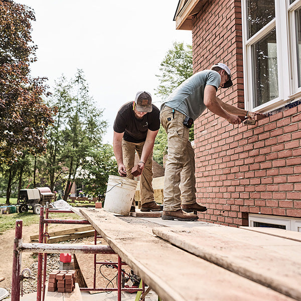 Two workers installing a brick wall outside a house.