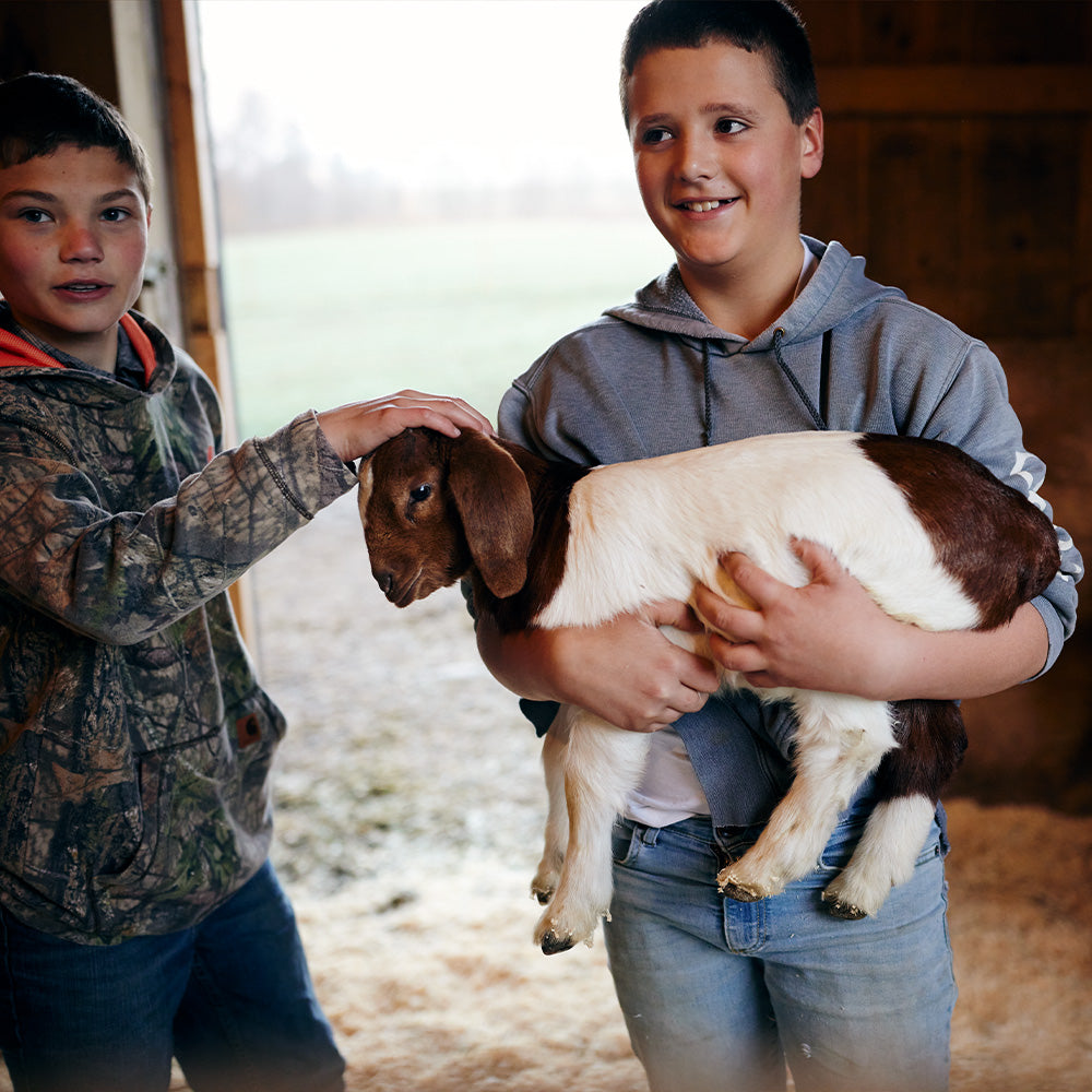 Two children holding a small goat in an indoor setting