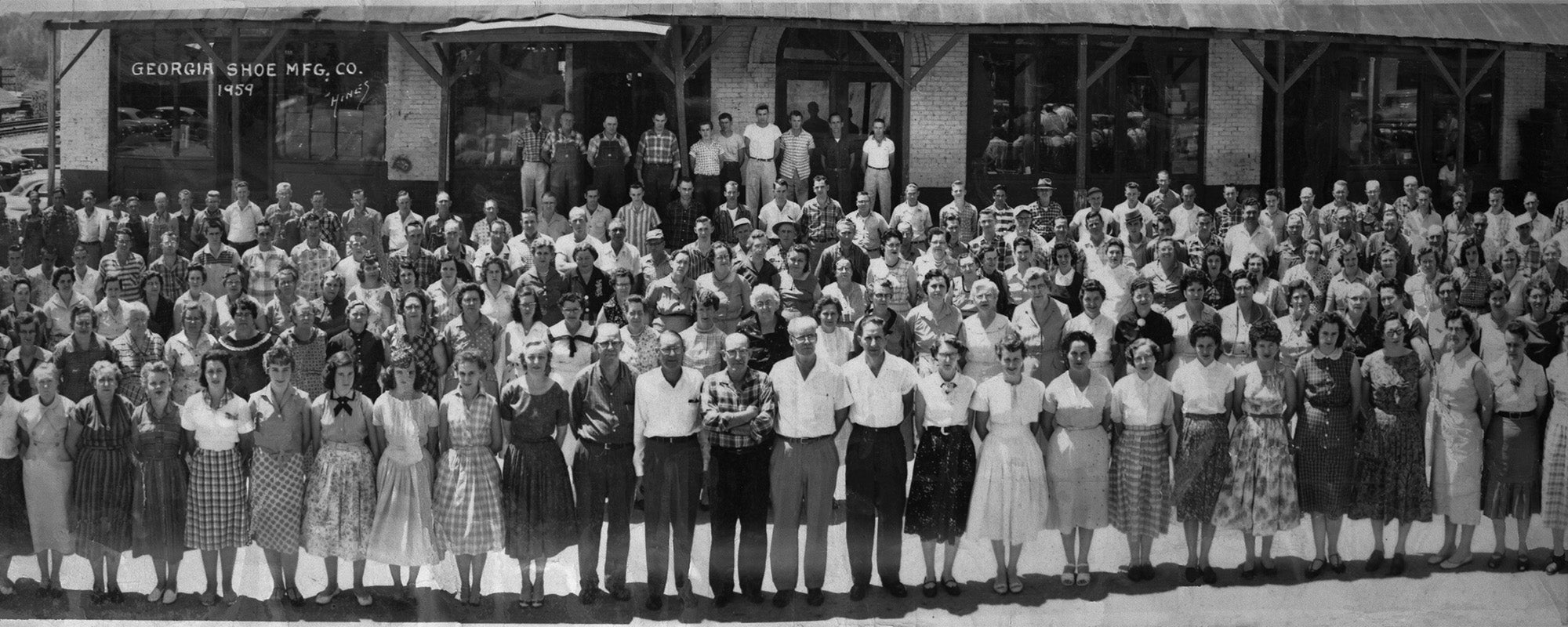 Vintage black and white photo of a large group of people posing in front of a building.