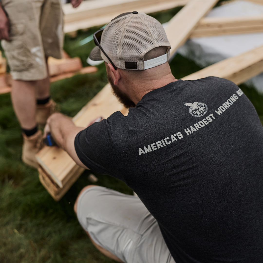 Person working on a wooden project outdoors, wearing a black t-shirt with text.