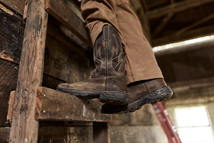 Person wearing brown work boots on a wooden ladder inside a building.