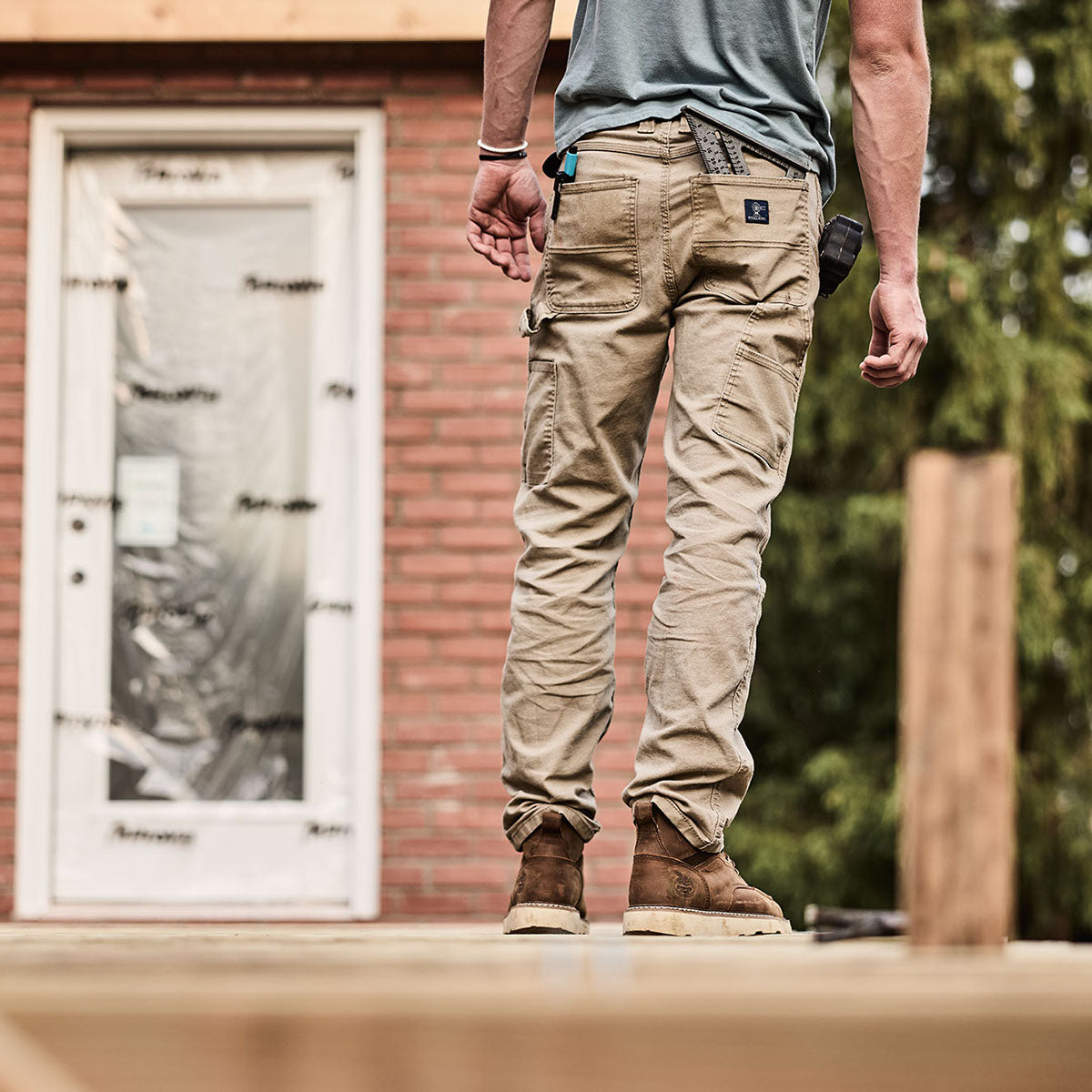 Person wearing beige pants standing on a wooden deck with a building in the background