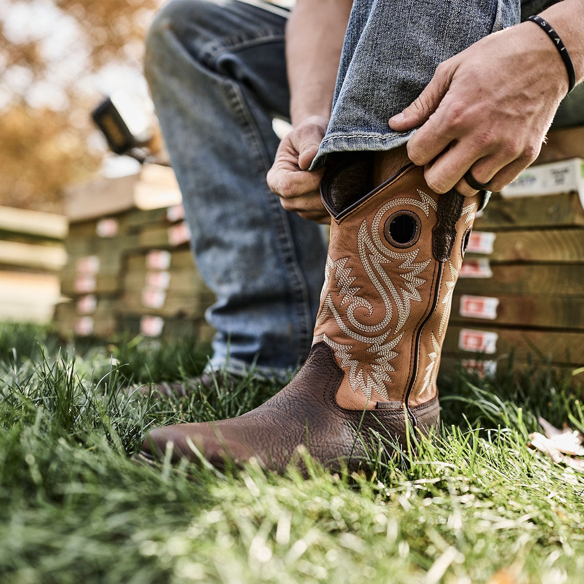Person wearing a brown cowboy boot with intricate white stitching on grass.