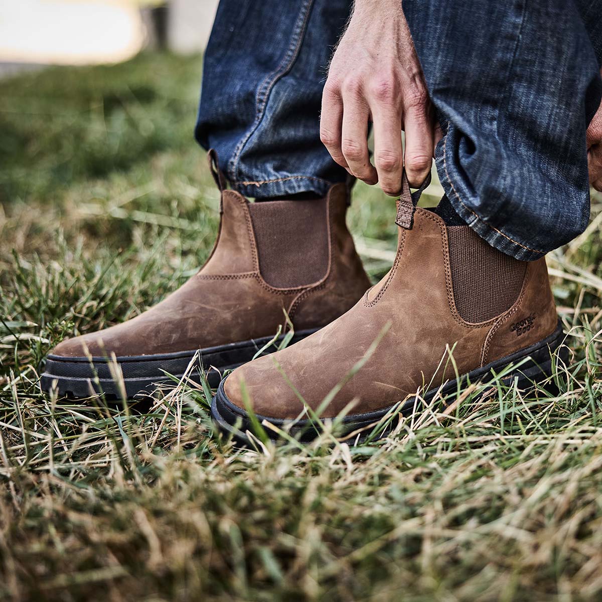 Brown boots worn with blue jeans on a grassy background